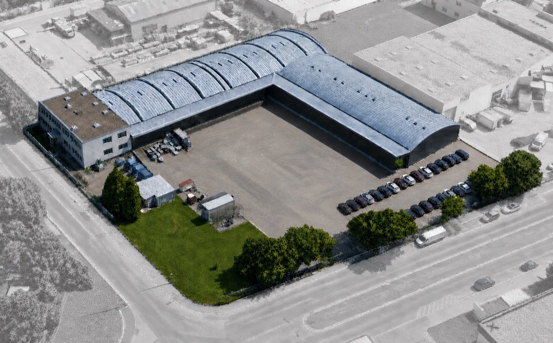 Oblique aerial view of the site: office building, two storage halls with barrel roofs, yard and planted verges.
